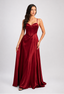 A woman modeling a floor-length burgundy evening gown with a structured velvet corset bodice and thin spaghetti straps, photographed against a light gray studio background.