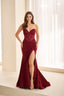 A woman models a strapless burgundy evening gown with a lace corset bodice, ruched draped skirt, and high thigh slit, standing in a bright indoor setting with white curtains.