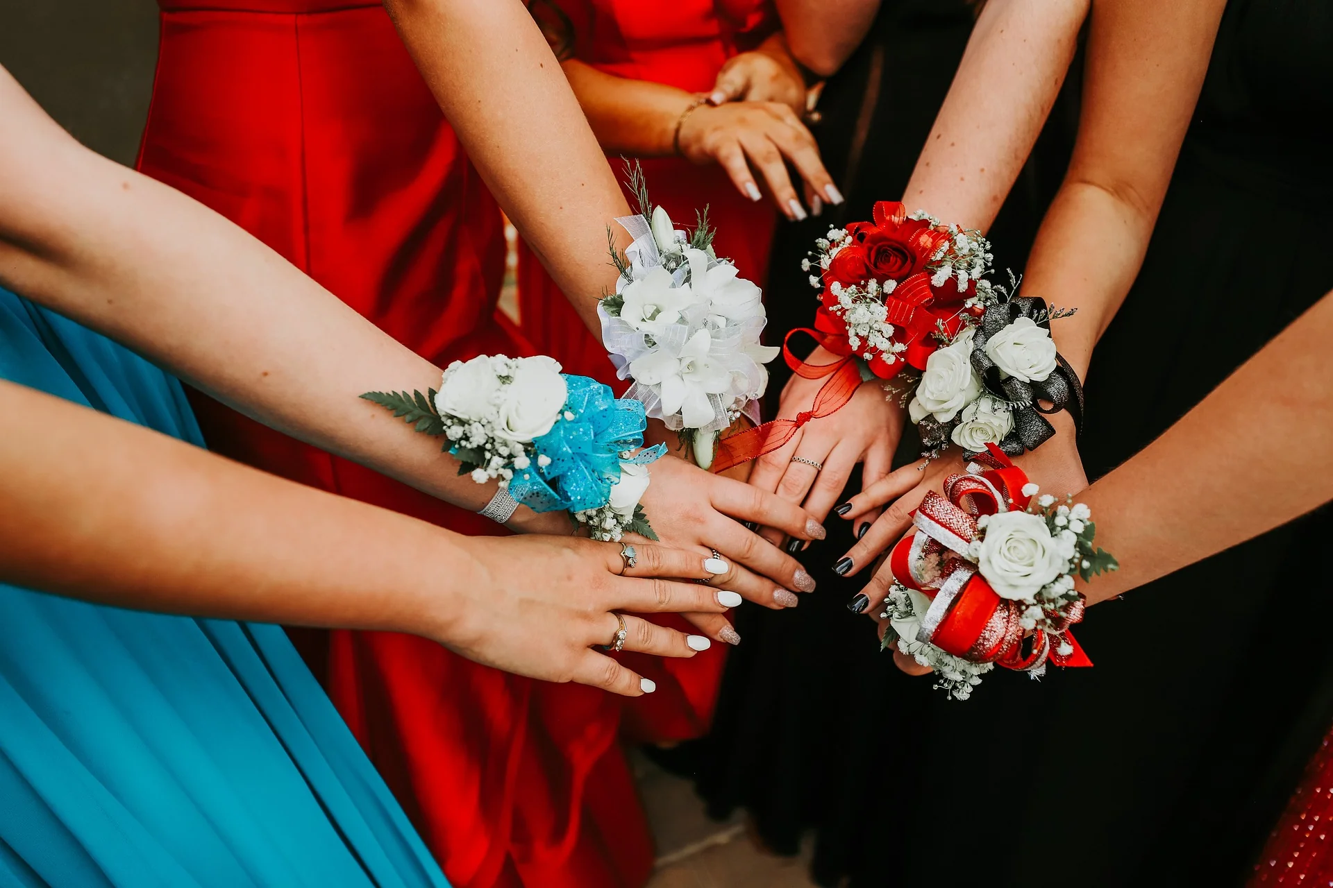 Colourful Prom Corsages on Wrist: Red, White, Blue, and Black Floral Designs A group of young women wearing traditional dresses display colourful prom corsages with red, white, black, and blue flower motifs.
